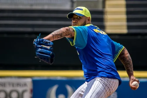 pitcher with blue jersey and yellow hat mid windup