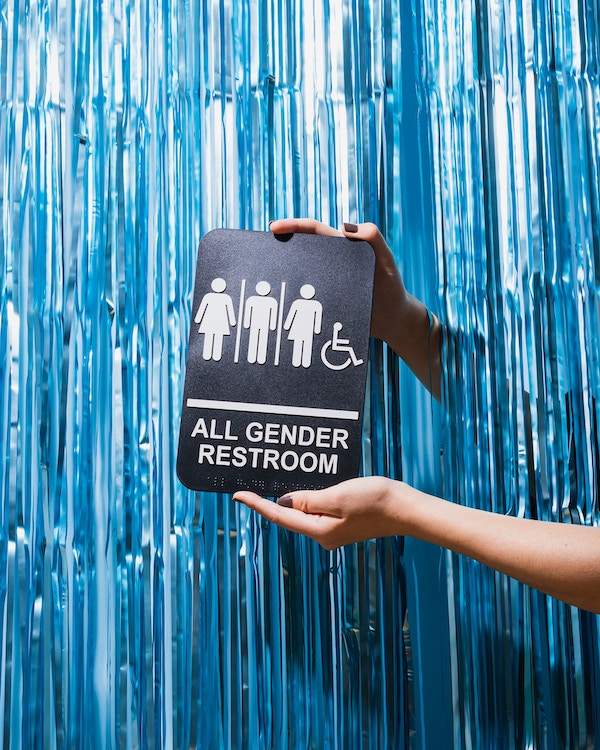 hands holding up all gender restroom sign with blue background 