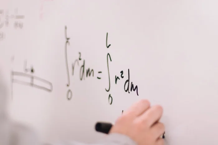 a math formula on a whiteboard with a hand writing it